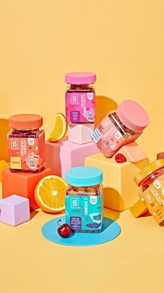 A visually striking, high-key studio photograph of various gummy vitamin bottles arranged on colorful geometric risers.